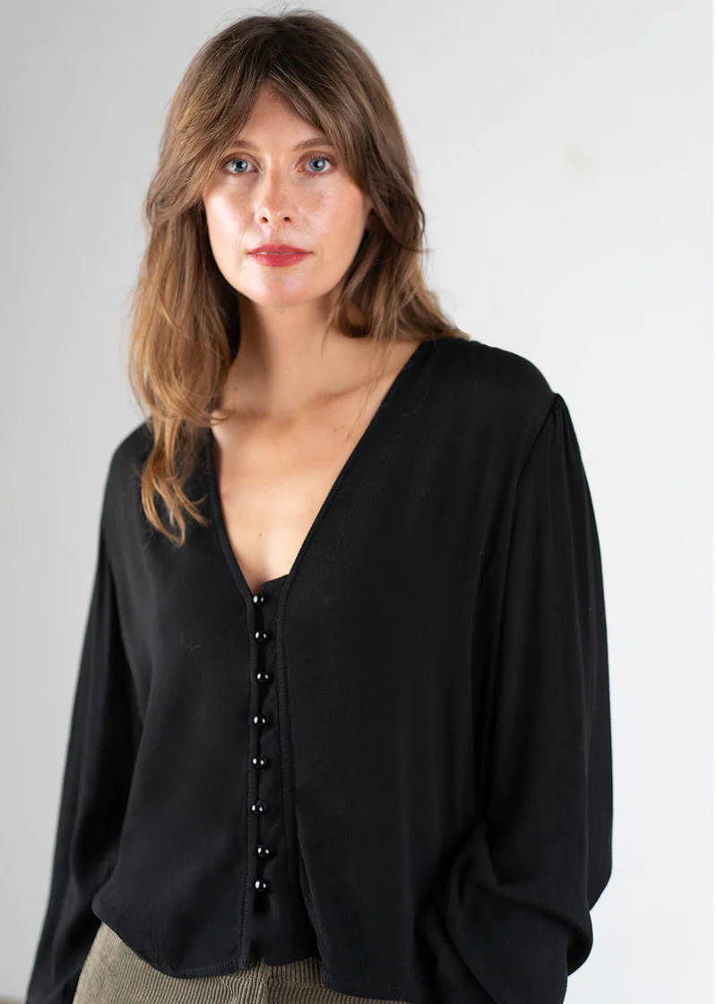 A model wearing an black coloured lightweight blouse with black buttons and long sleeves with elasticated cuffs