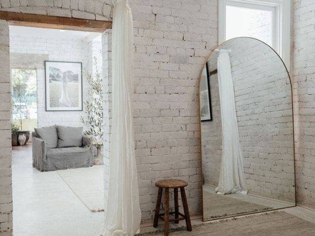 Weiß gestrichener Sichtziegel und Bogenspiegel im minimalistischen Umkleideraum