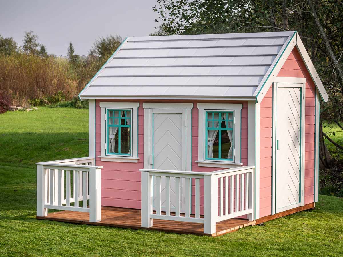 Pink Outdoor Playhouse Unicorn with white metal roof and white doors on green lawn in a backyard by WholeWoodPlayhouses