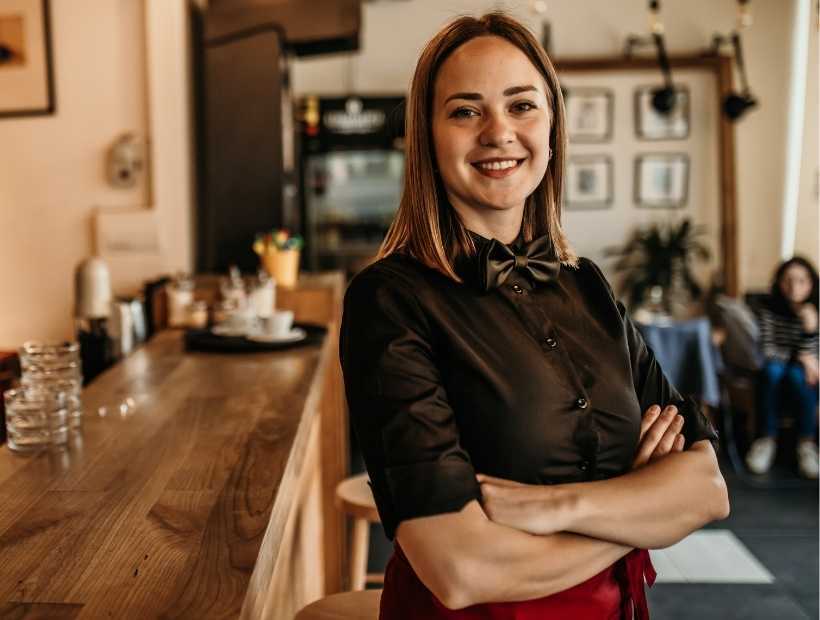 Waitress standing by bar wearing a black dress shirt and black bow tie