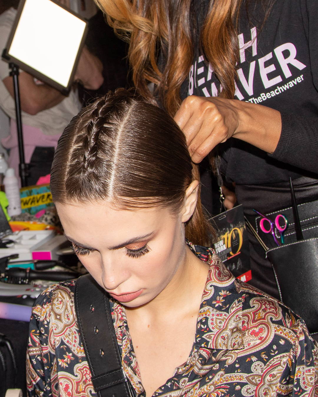Image of a model getting her hair styles into a sleek braided look backstage at NYFW