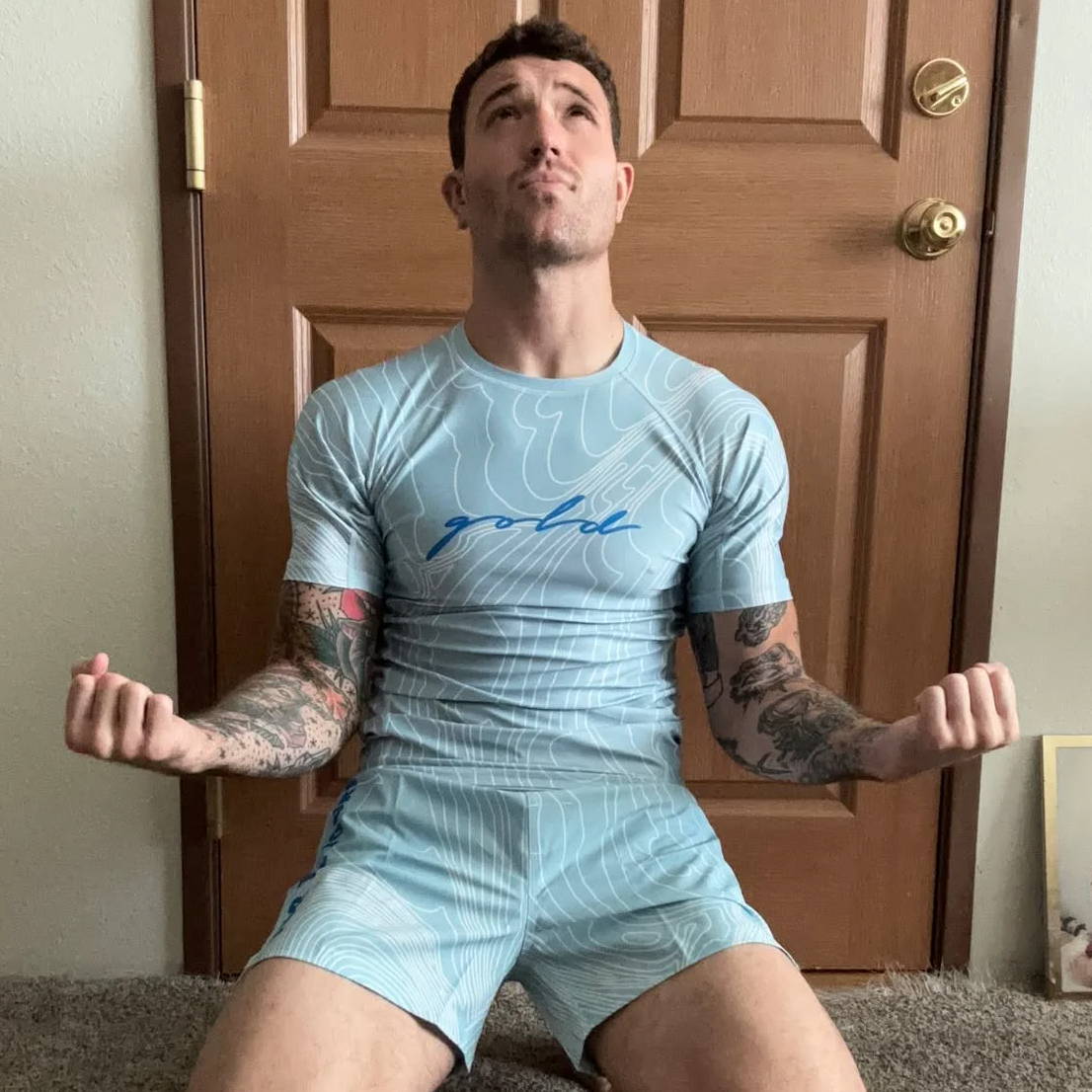 Person in blue athletic wear kneeling on carpet, arms raised in expression.