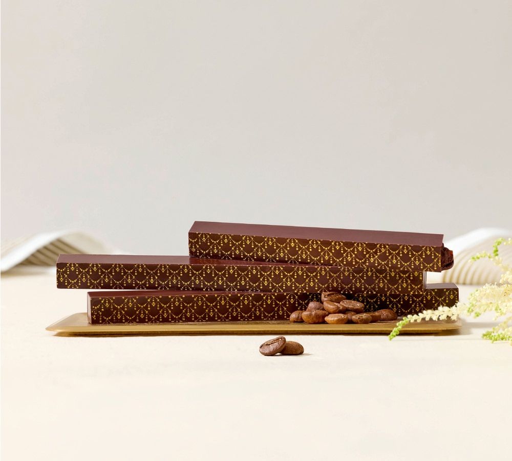 Three chocolate bars with decorative packaging and cocoa beans on a wooden board.