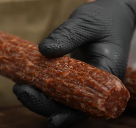 A hand in a black glove holding a piece of sausage.
