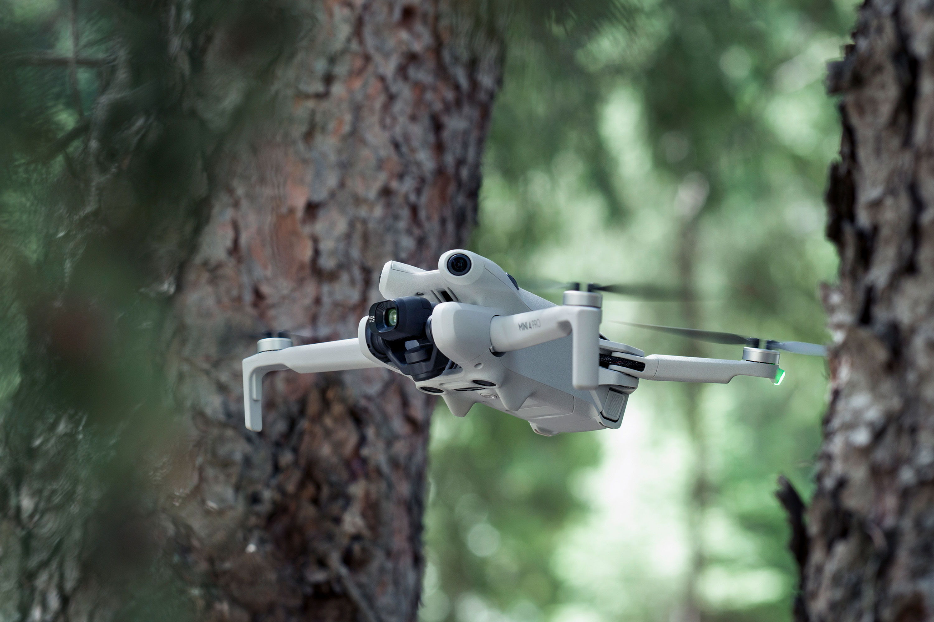 A DJI Mini 4 Pro flies through a forested area