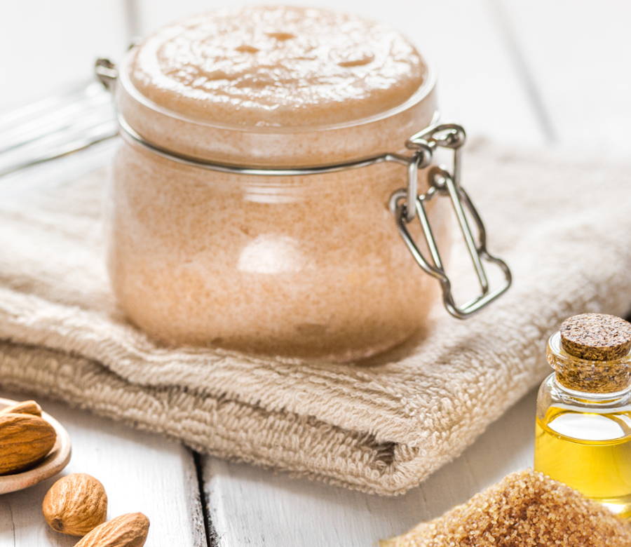 a glass jar of DIY body scrub on top of a folded towel with brown sugar and almonds around it