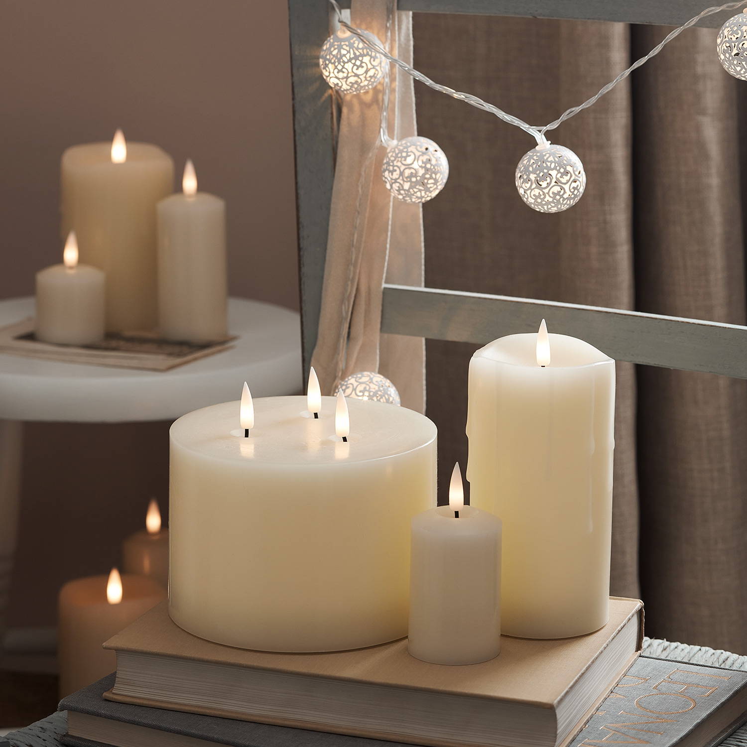 3 ivory LED candles on top of a chair with fairy lights and more candles in the background.