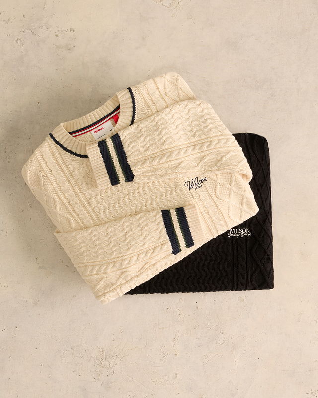 Two sweaters, one cream and one black, stacked on a light surface.