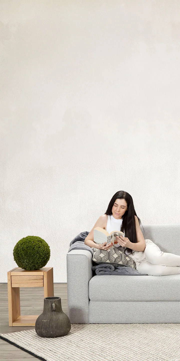 A woman lounging on a new Zeek Silver Sofa Bed reading a book.