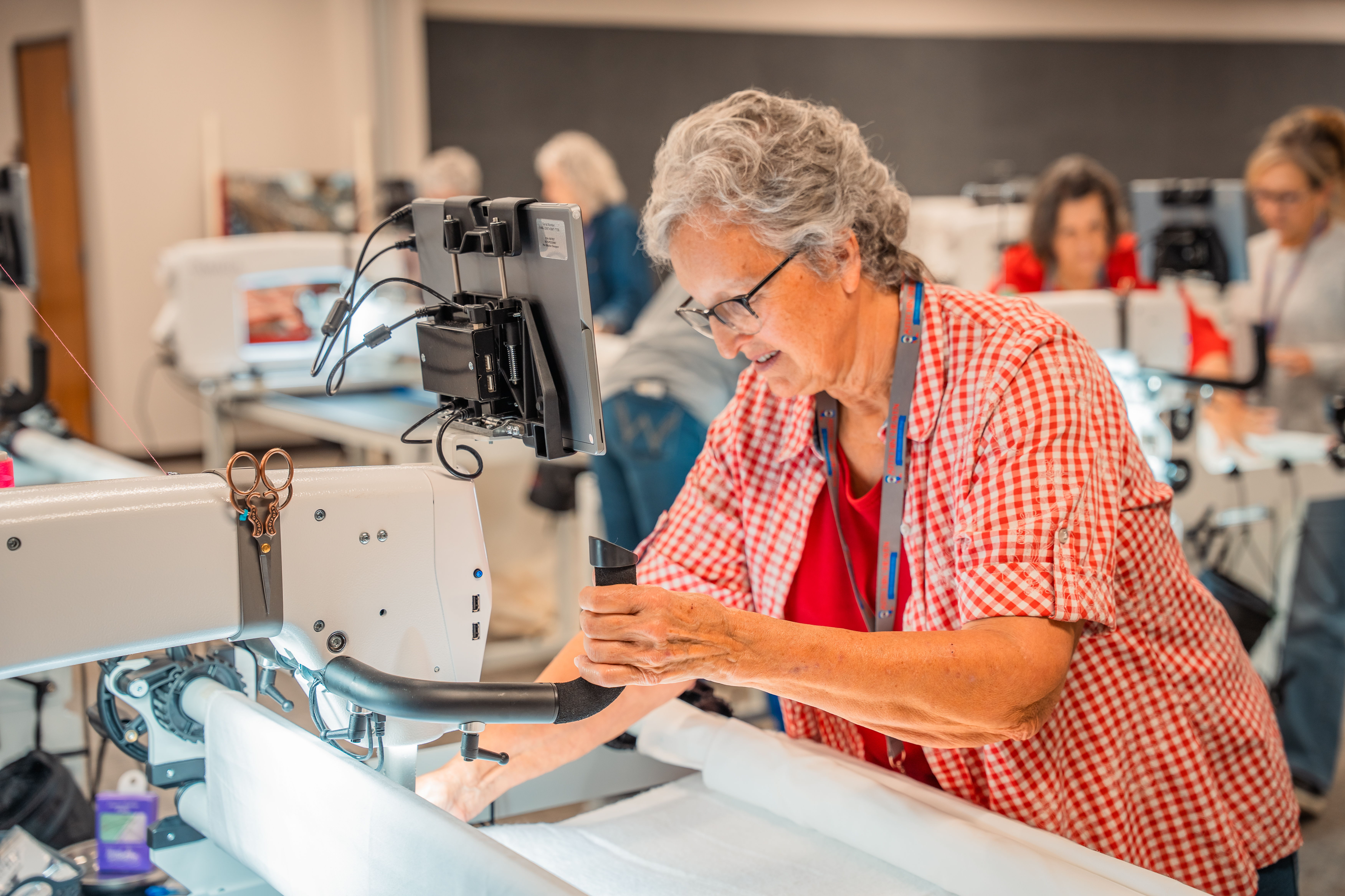 Elderly woman sewing at a machine in a bright, collaborative workspace.