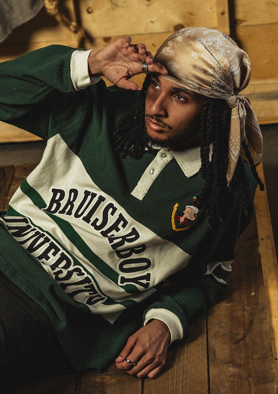 Person wearing a green and white shirt with a bandana, sitting on wooden floor.