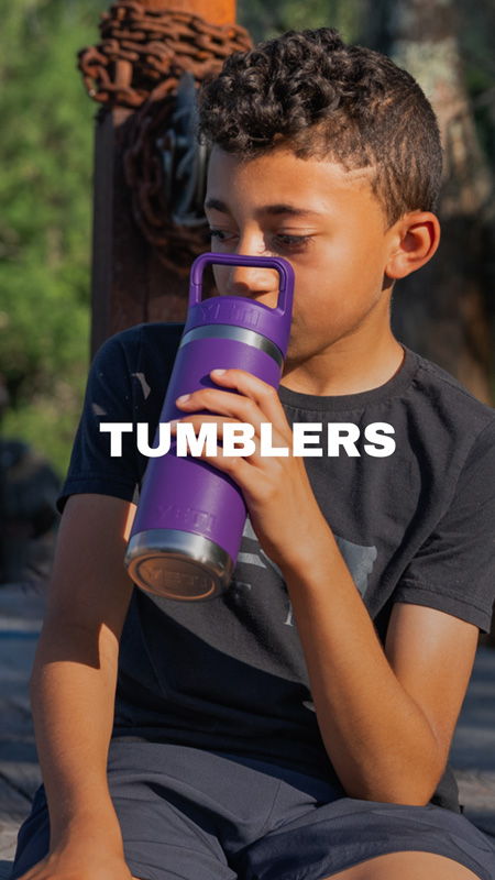 Boy drinking from a purple tumbler outdoors.