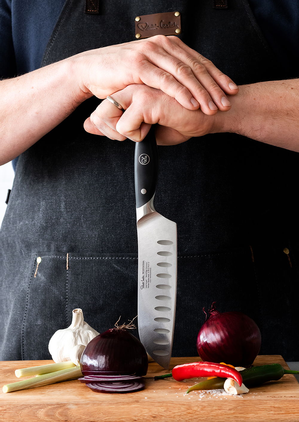 Hands holding the Professional Santoku knife over chopped vegetables on a wooden cutting board.