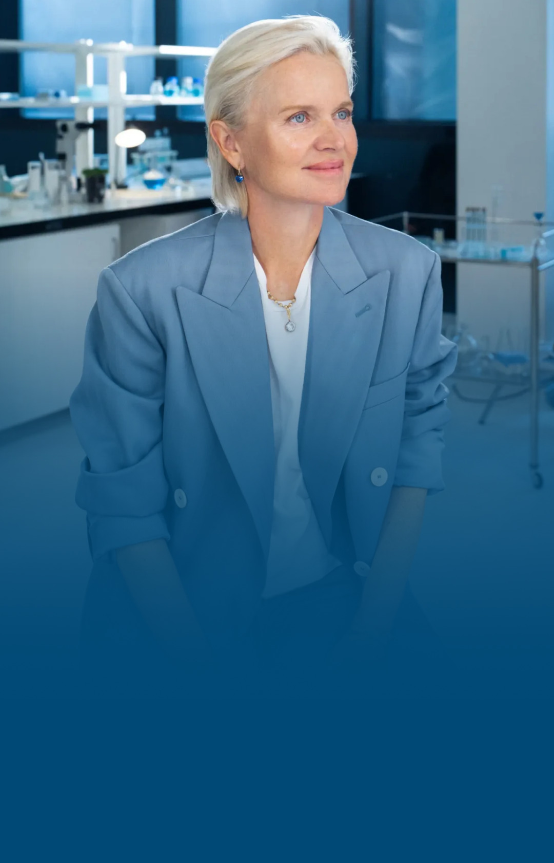 A smiling woman in a lab setting, wearing a blue blazer.