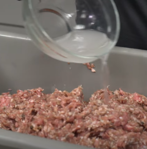 Pouring liquid into a container of ground meat.