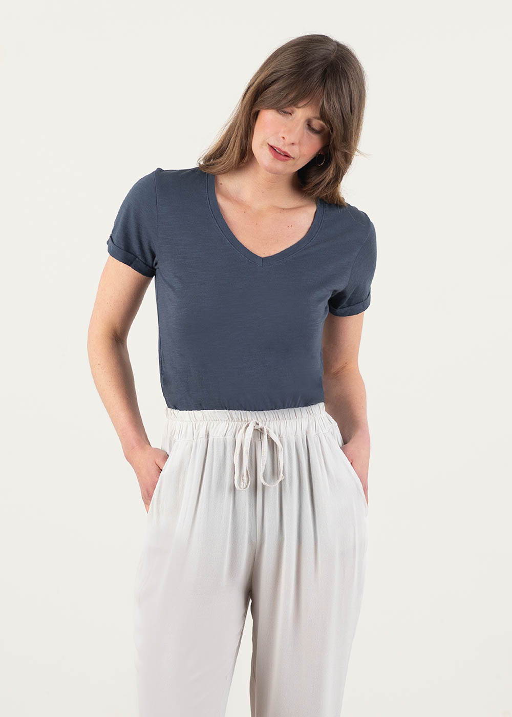 A model wearing a blue - grey v neck short sleeved t shirt with oatmeal trousers