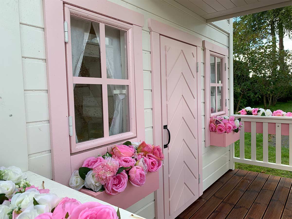 Close up of front pink fishbone door, safety glass windows and pink flower boxes of 2-Story Outdoor Playhouse Princess by WholeWoodPlayhouses