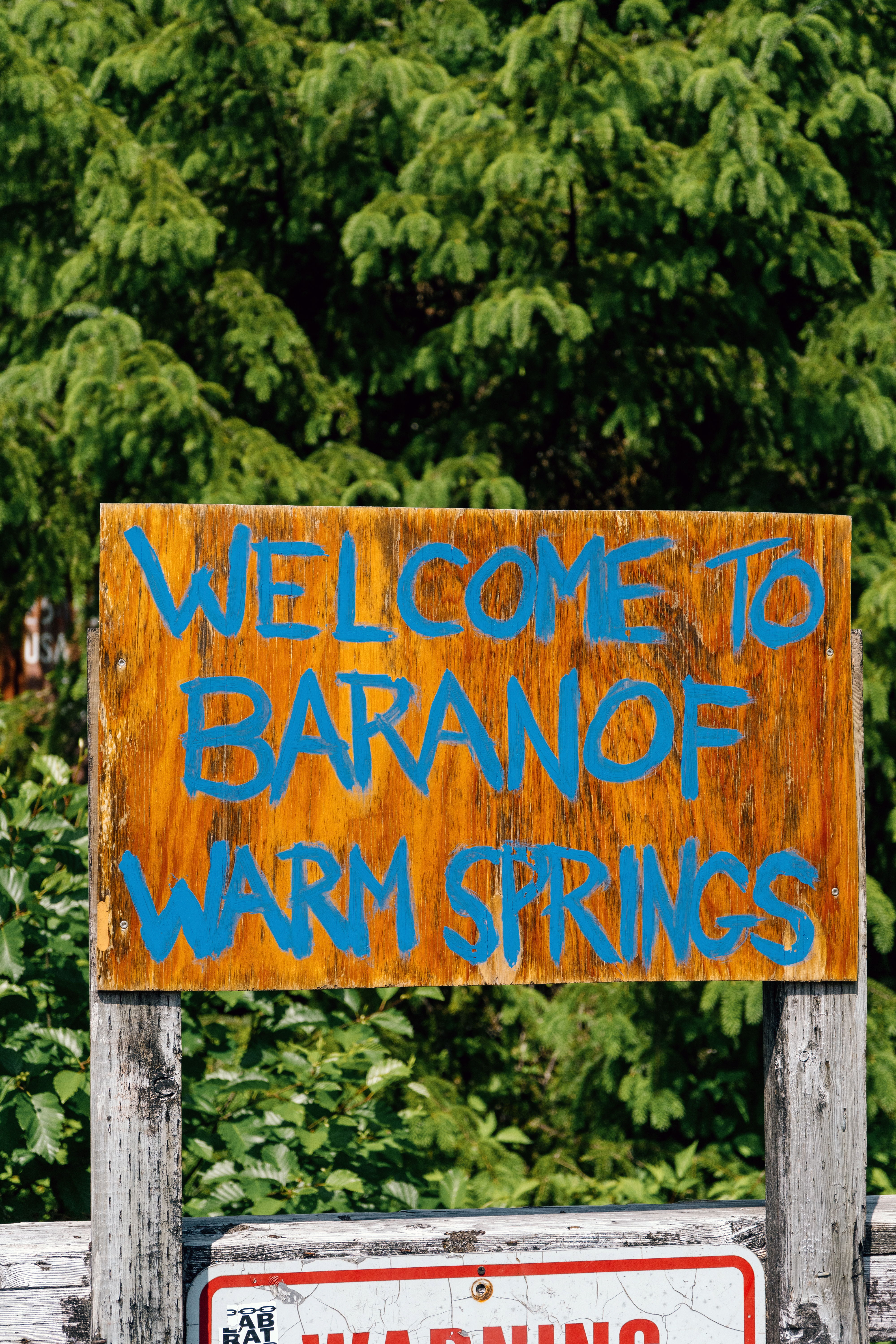 Welcome to Baranof Warm Springs sign surrounded by greenery.