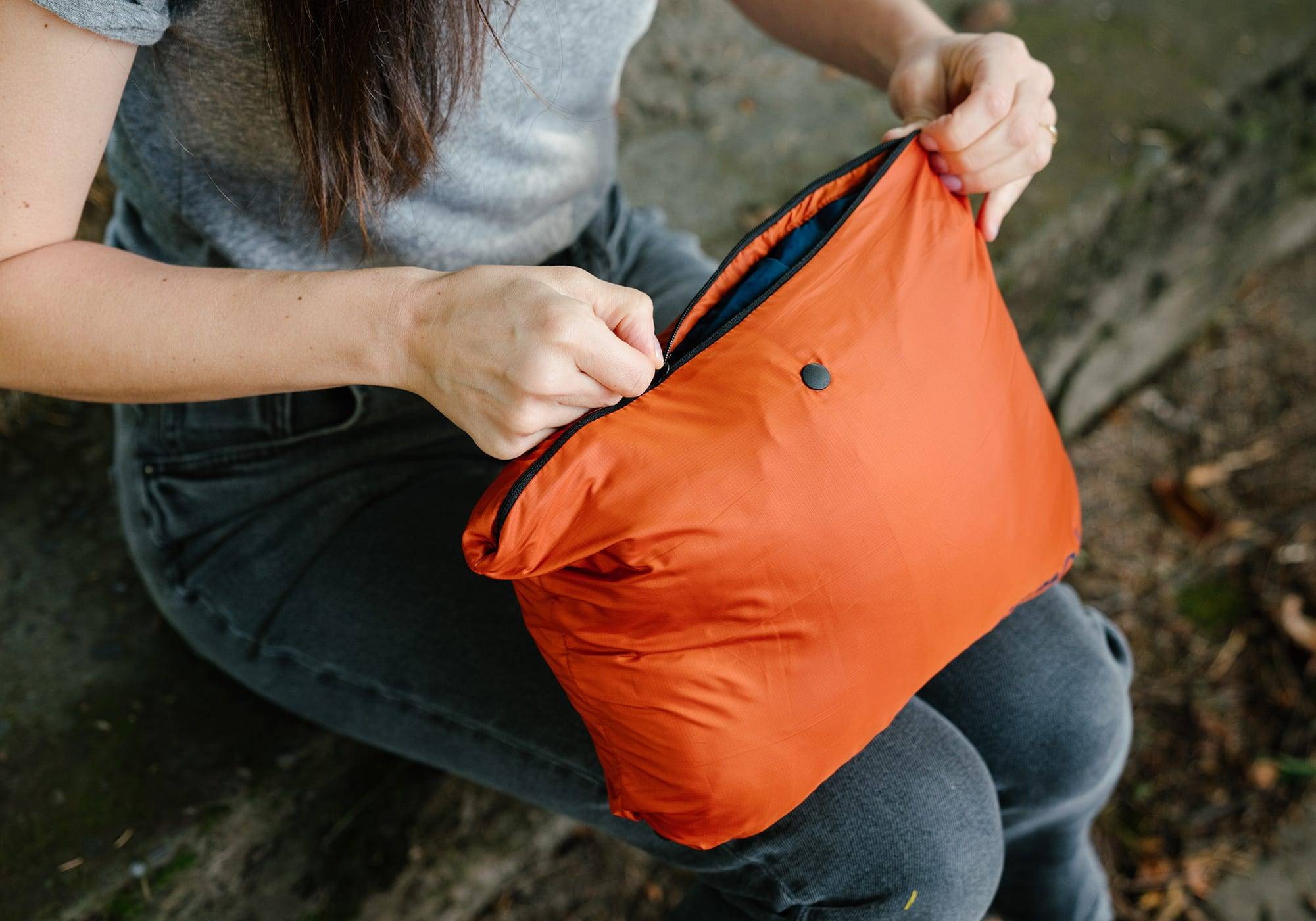 Woman packing Rumpl poncho into it's pocket to a camping pillow