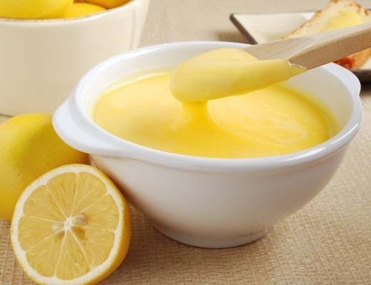 Bowl of lemon curd with fresh lemons beside it.