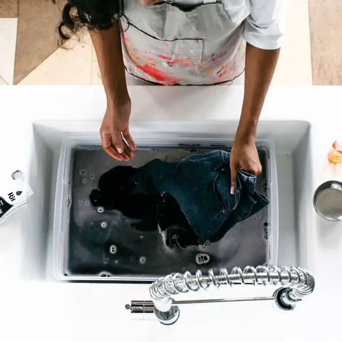 Person washing clothes in a sink filled with water and bubbles.