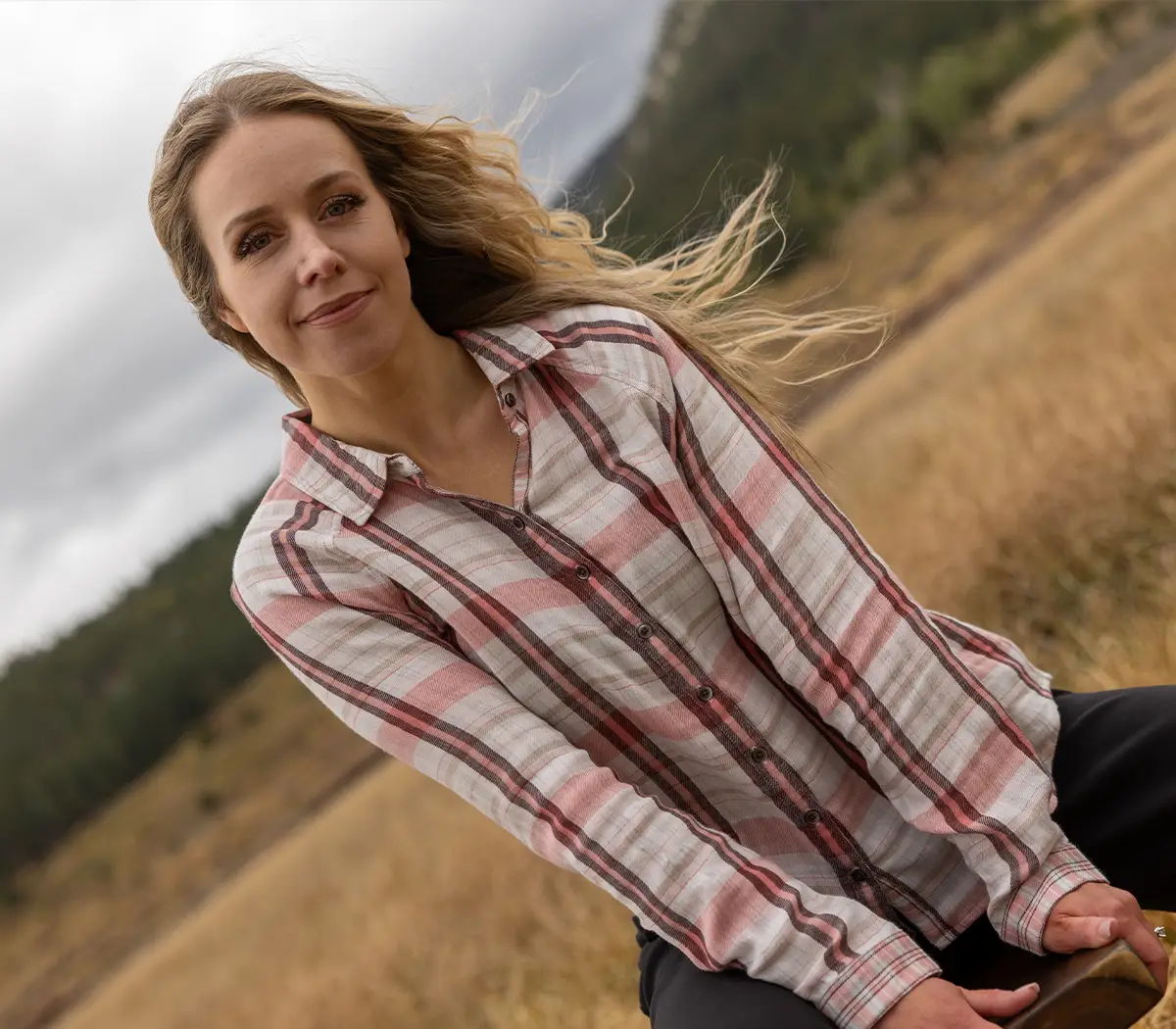 Young woman in a plaid shirt sitting in a field with grass.