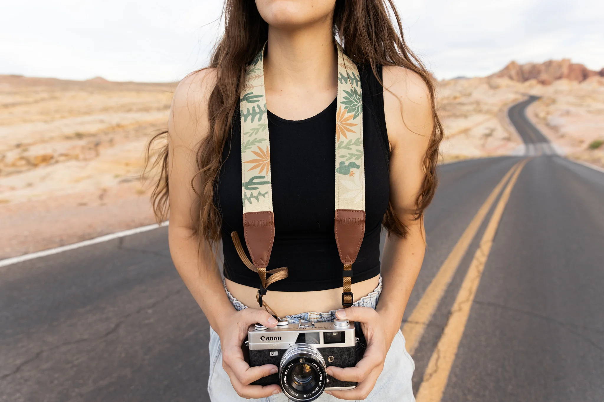 Woman wearing a cactus neck camera strap while standing on a road practicing travel photography. 