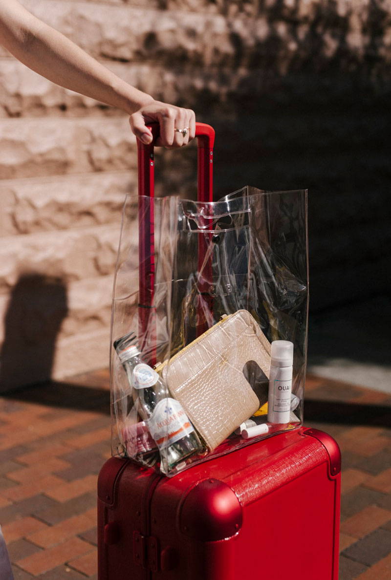 CALPAK Clear Tote from the Neck Pillow and Eye Mask Set and Jen Atkin x CALPAK Carry-On in red.