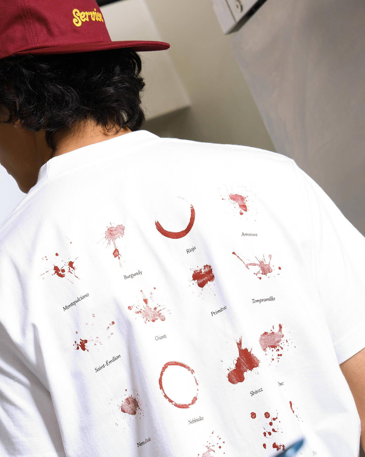 A look book image of a model wearing the Service Works Wine Spill T-Shirt in white.