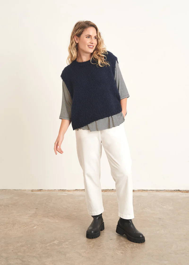 A model wearing a dark blue sleeveless sweater over a striped top, white trousers and black chunky boots