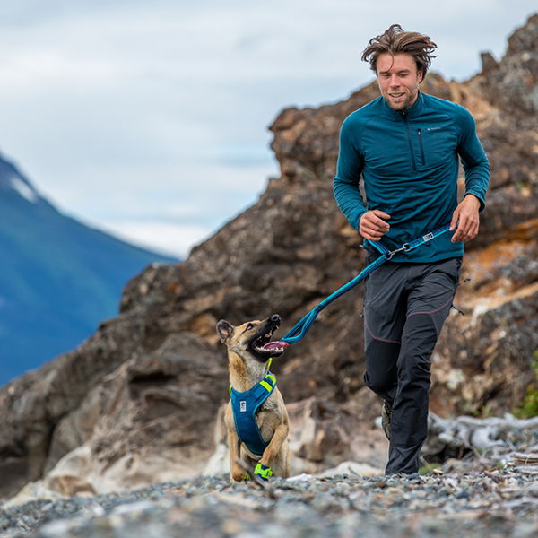 A man runs with a dog on a rocky trail.
