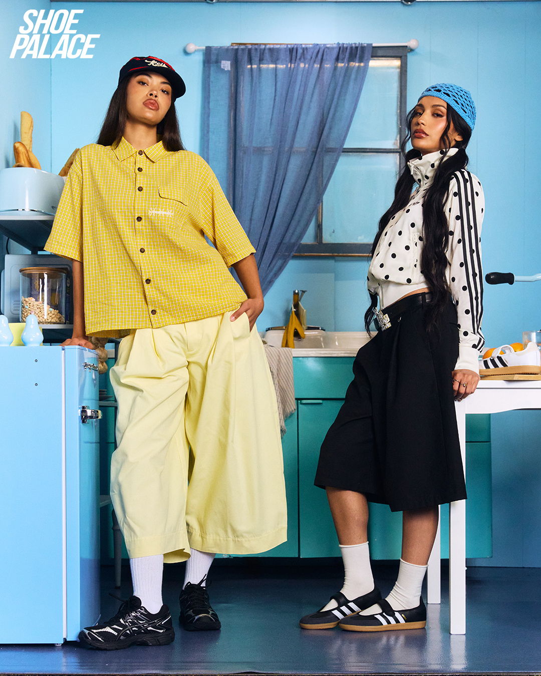 Two women in stylish outfits posing in a colorful kitchen setting.