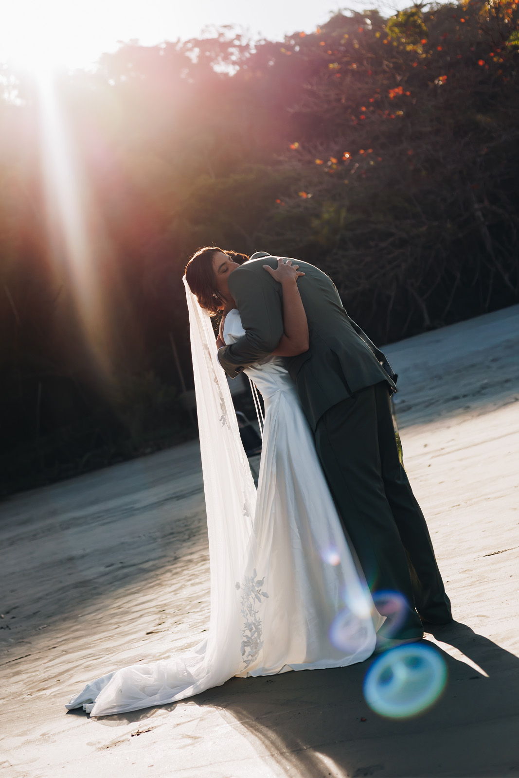 A couple embraces on a beach, sunlight shining in the background.