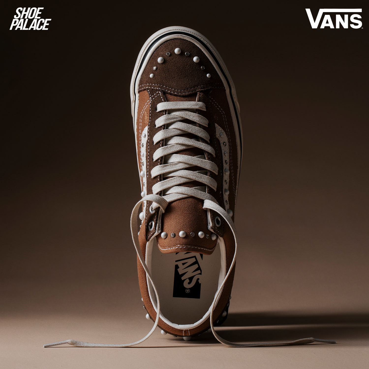 Brown Vans sneaker with white laces, displayed against a dark background.