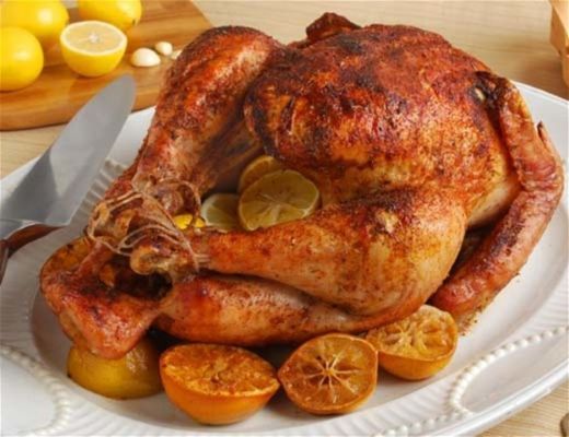 Roasted turkey with lemon slices on a white platter.