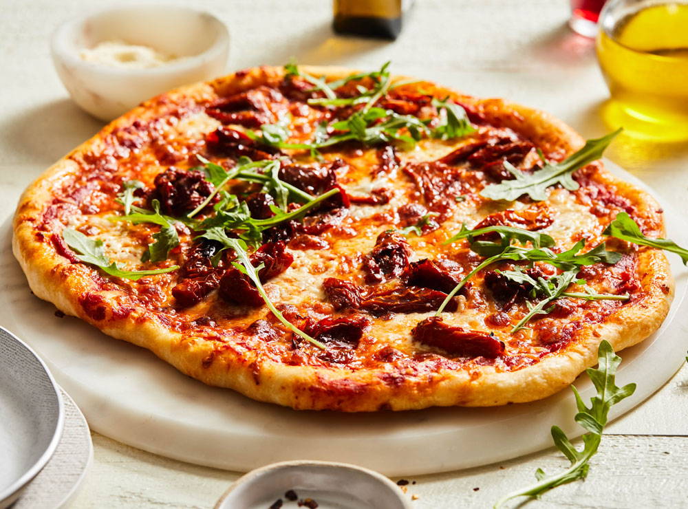 Baked pizza topped with cheese, arugula and sun-dried tomatoes