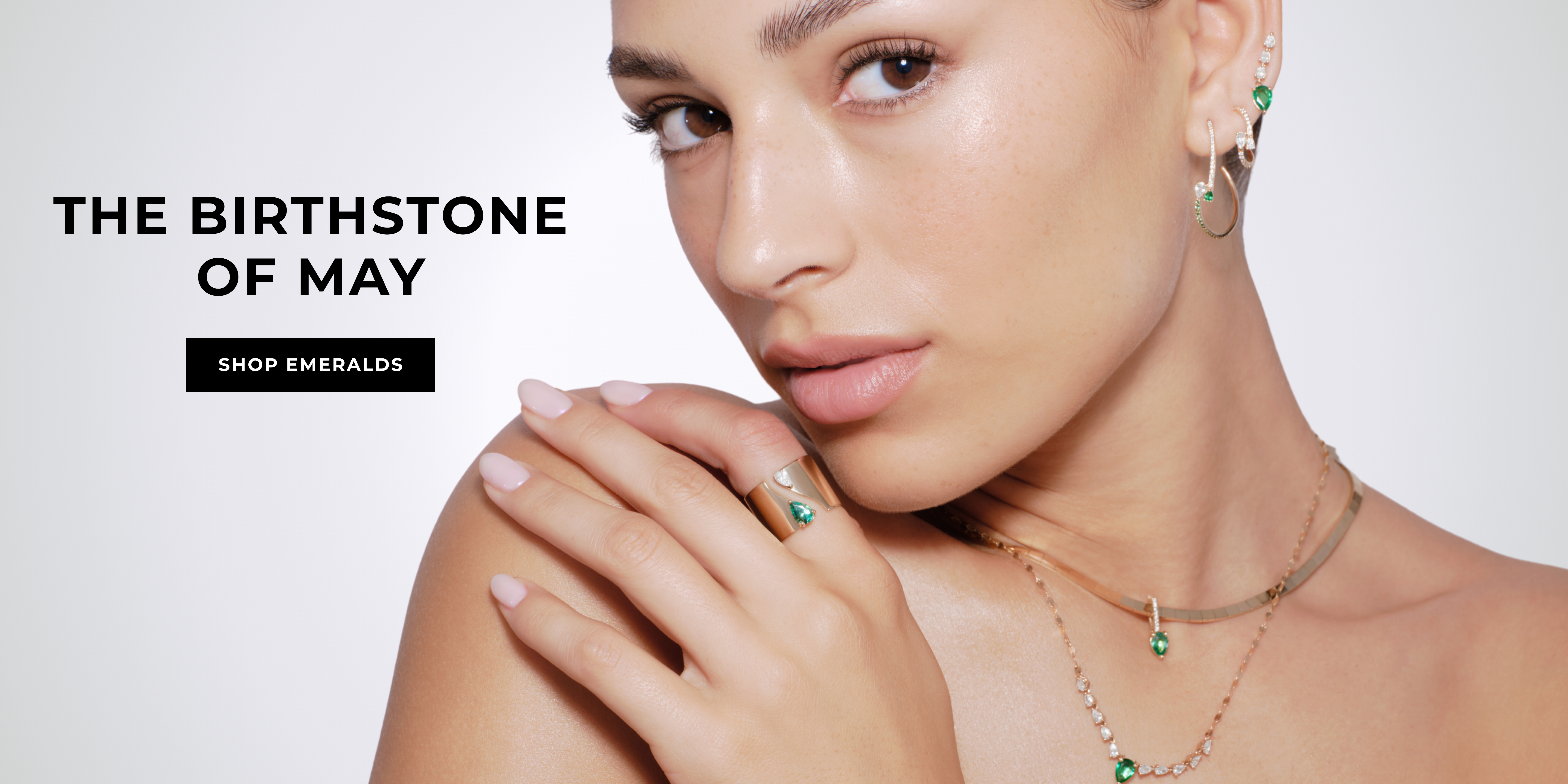 A woman showcasing jewelry featuring the birthstone of May, emerald.