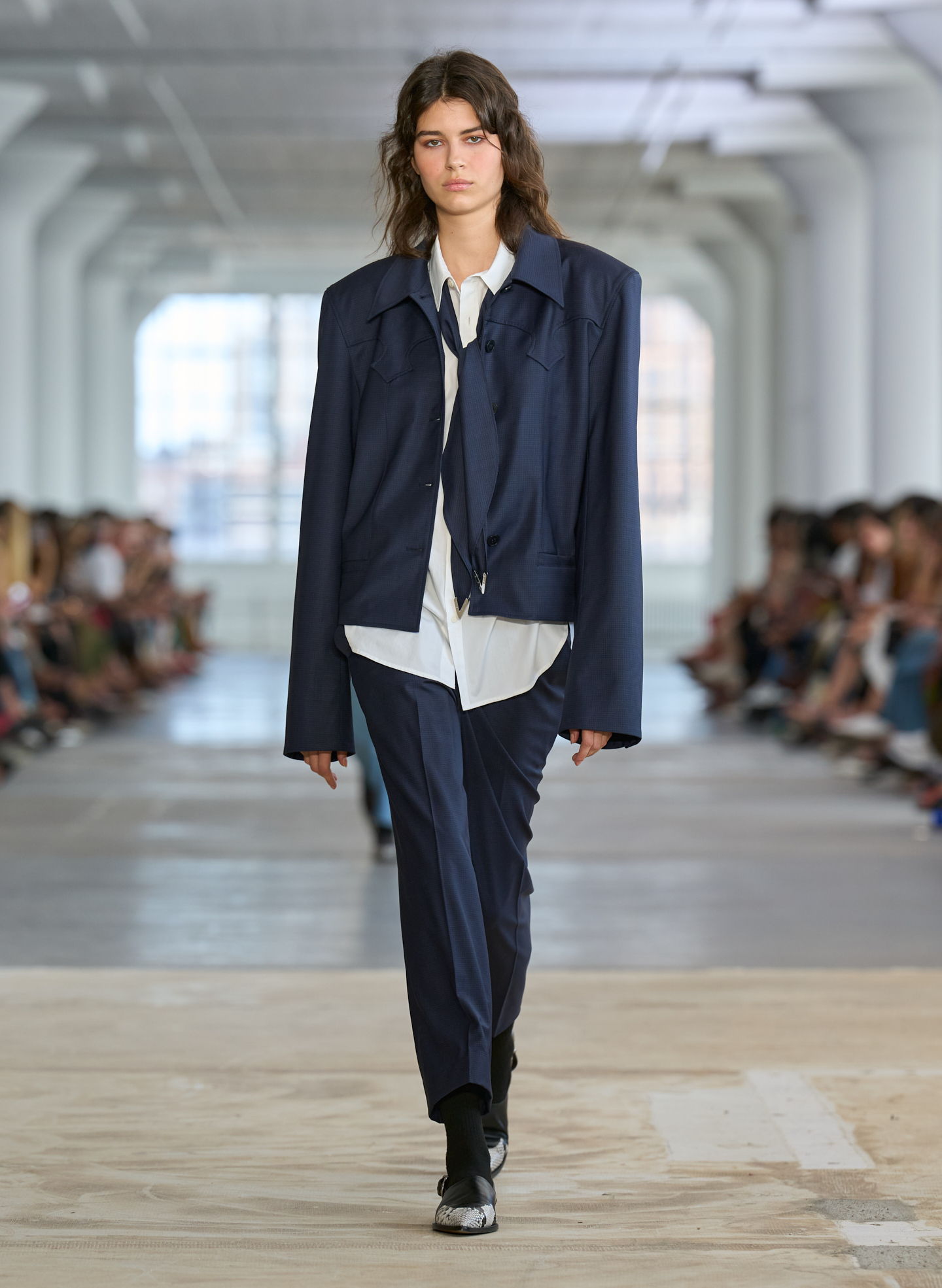Model walking down runway in oversized navy outfit.
