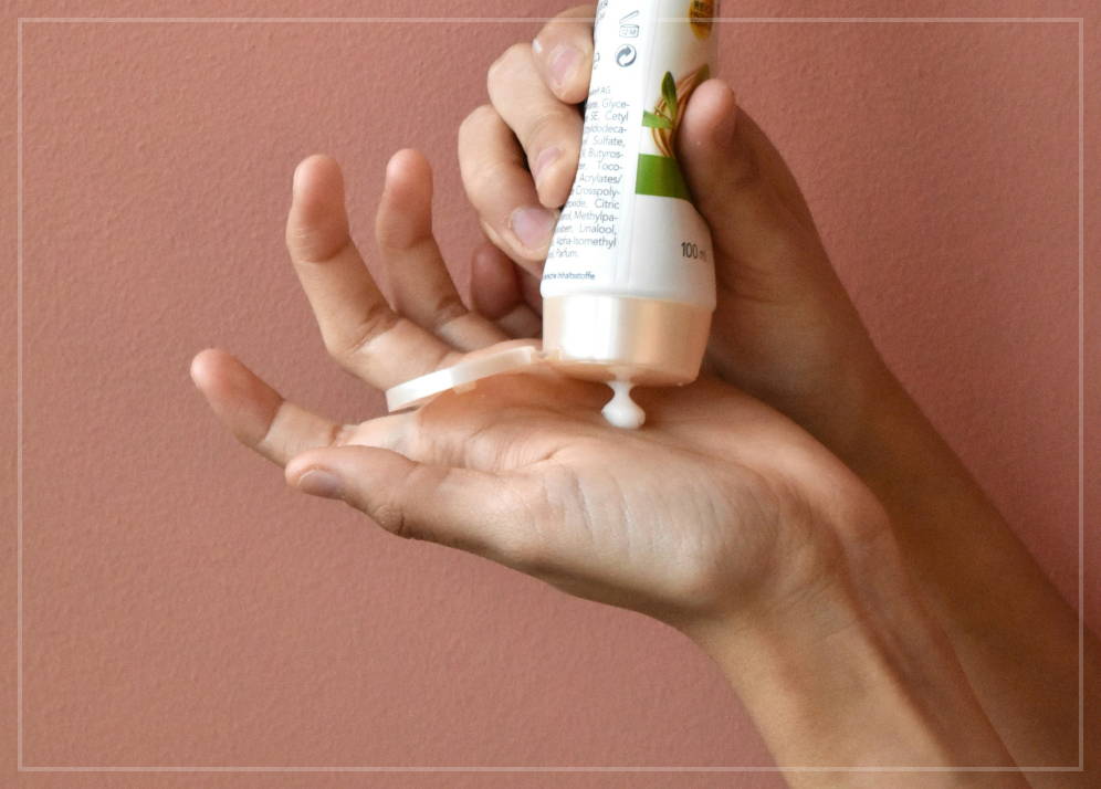 A pair hands, one of which is holding a bottle of moisturizing cream and is squirting a glob of it into the palm of the other hand