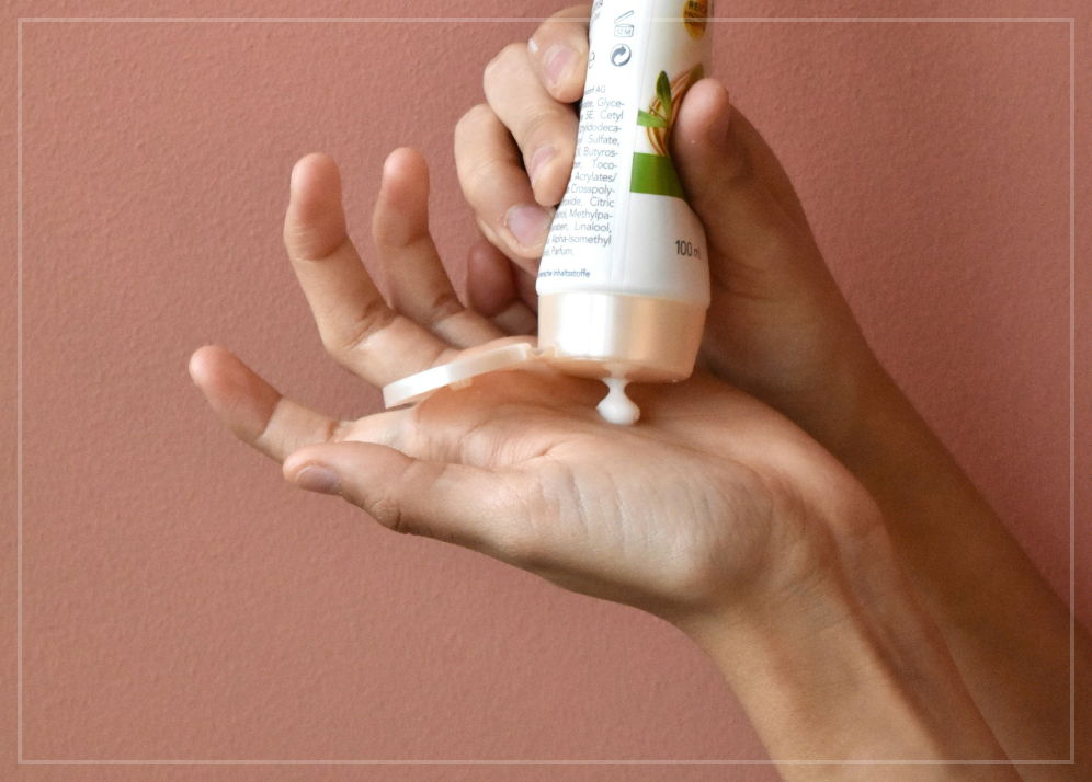 A pair hands, one of which is holding a bottle of moisturizing cream and is squirting a glob of it into the palm of the other hand