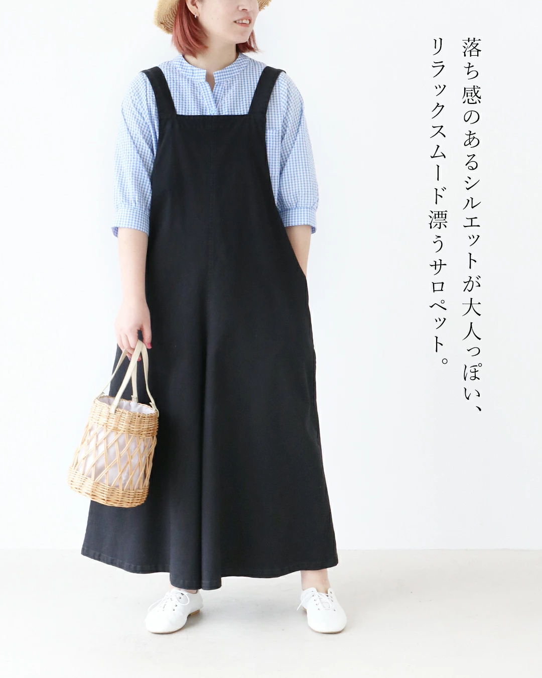 Woman in a black dress holding a woven bag, standing against a light background.