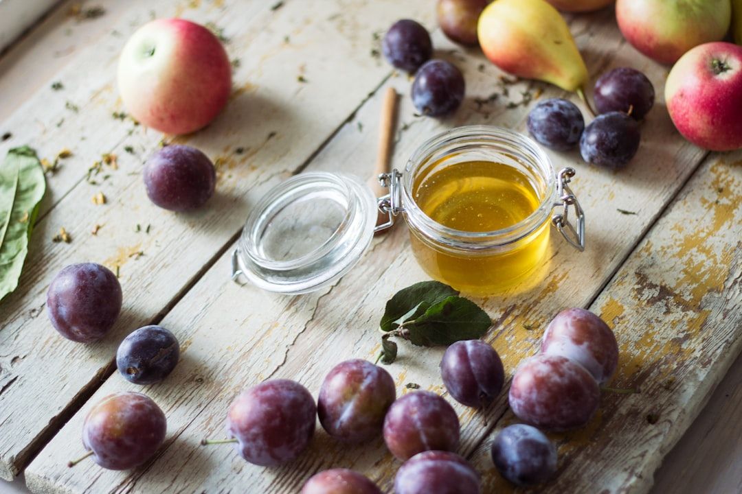 clear glass jar with yellow liquid beside red round fruits