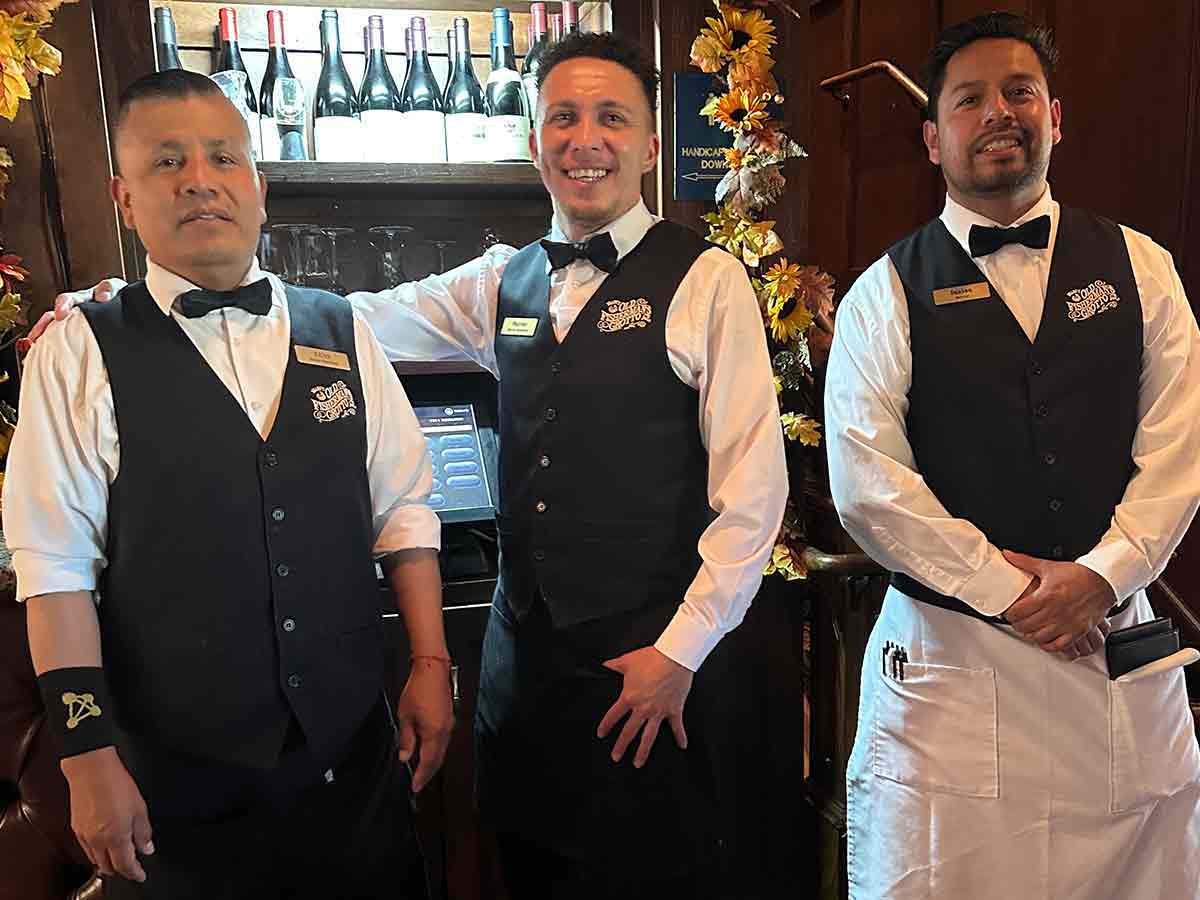 Three waiters wearing black bow ties and vests