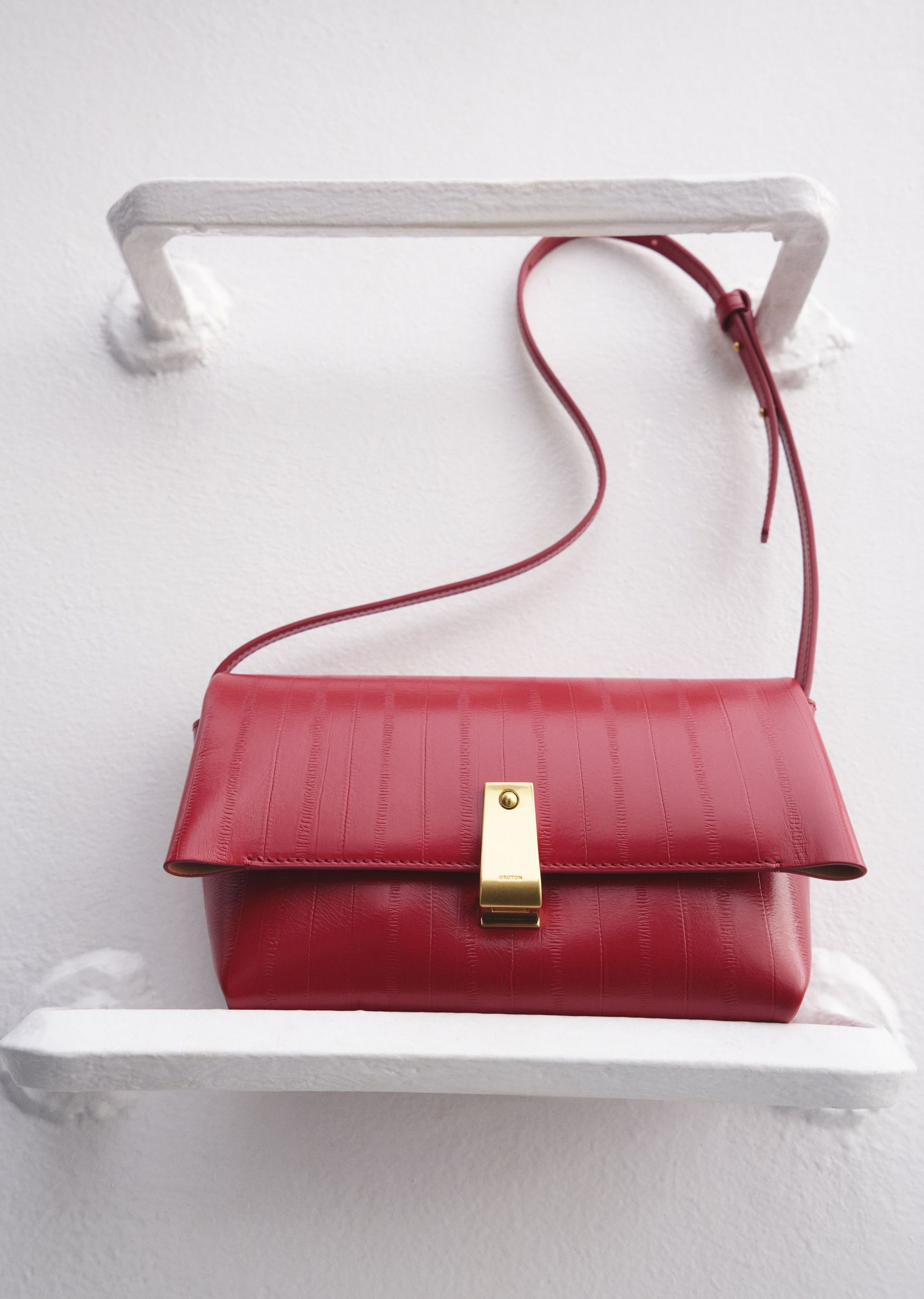 Red leather handbag displayed on a white shelf.
