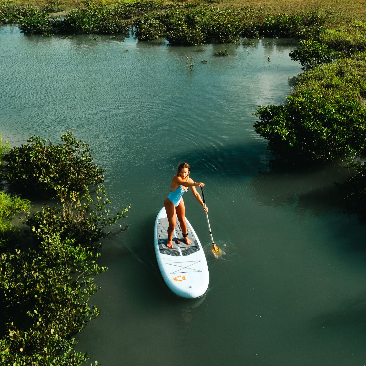 A woman paddleboarding on a calm waterway surrounded by greenery.