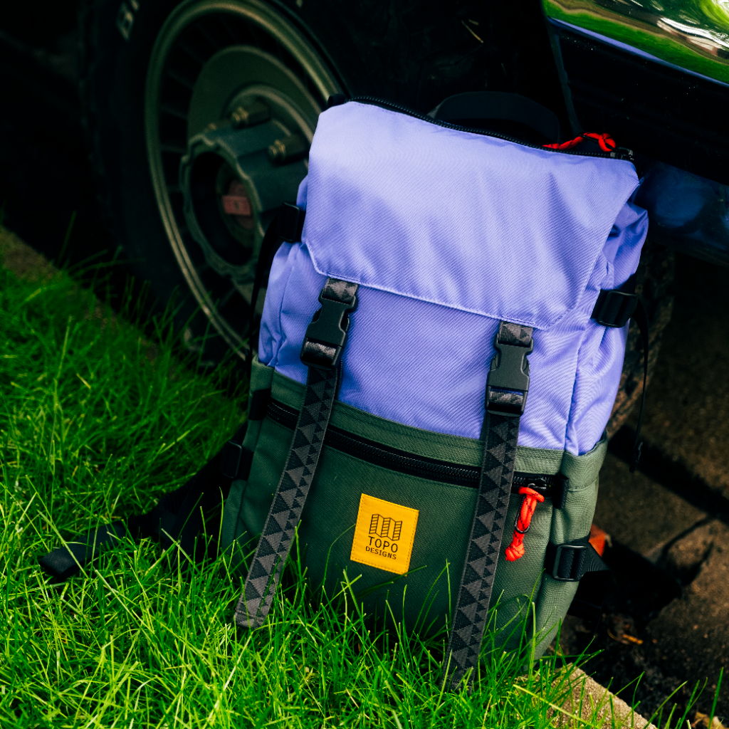 A colorful backpack resting on green grass near a vehicle tire.