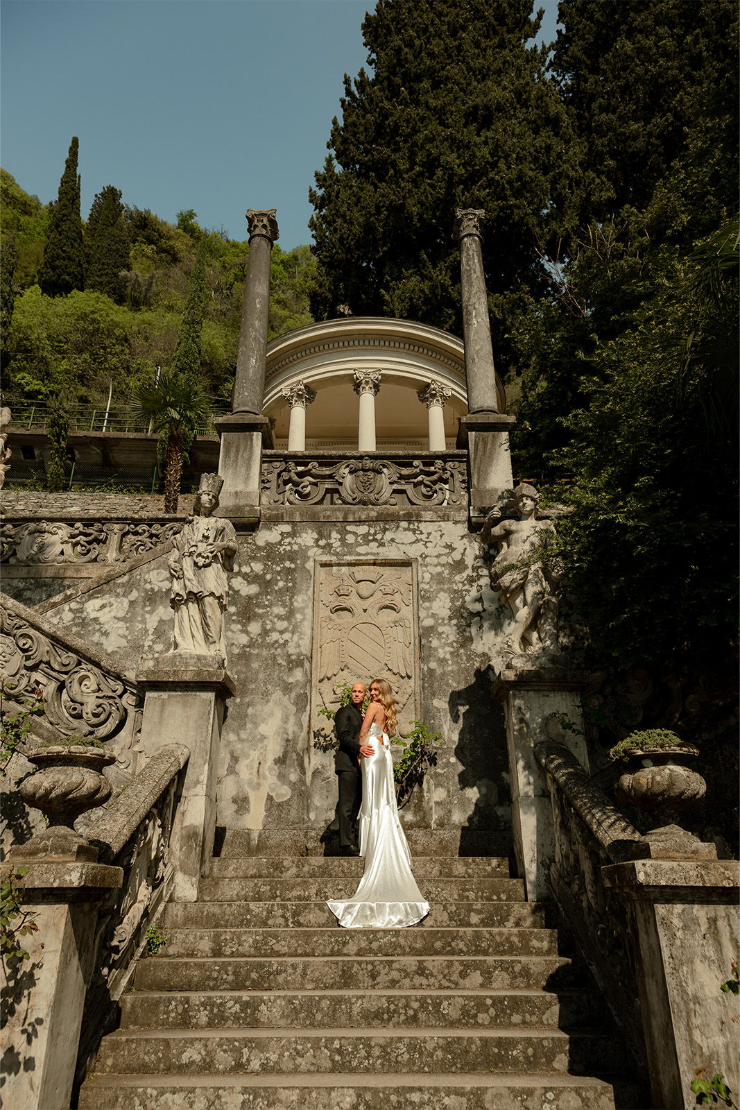 Bride in a white dress on stone steps at a historic site.