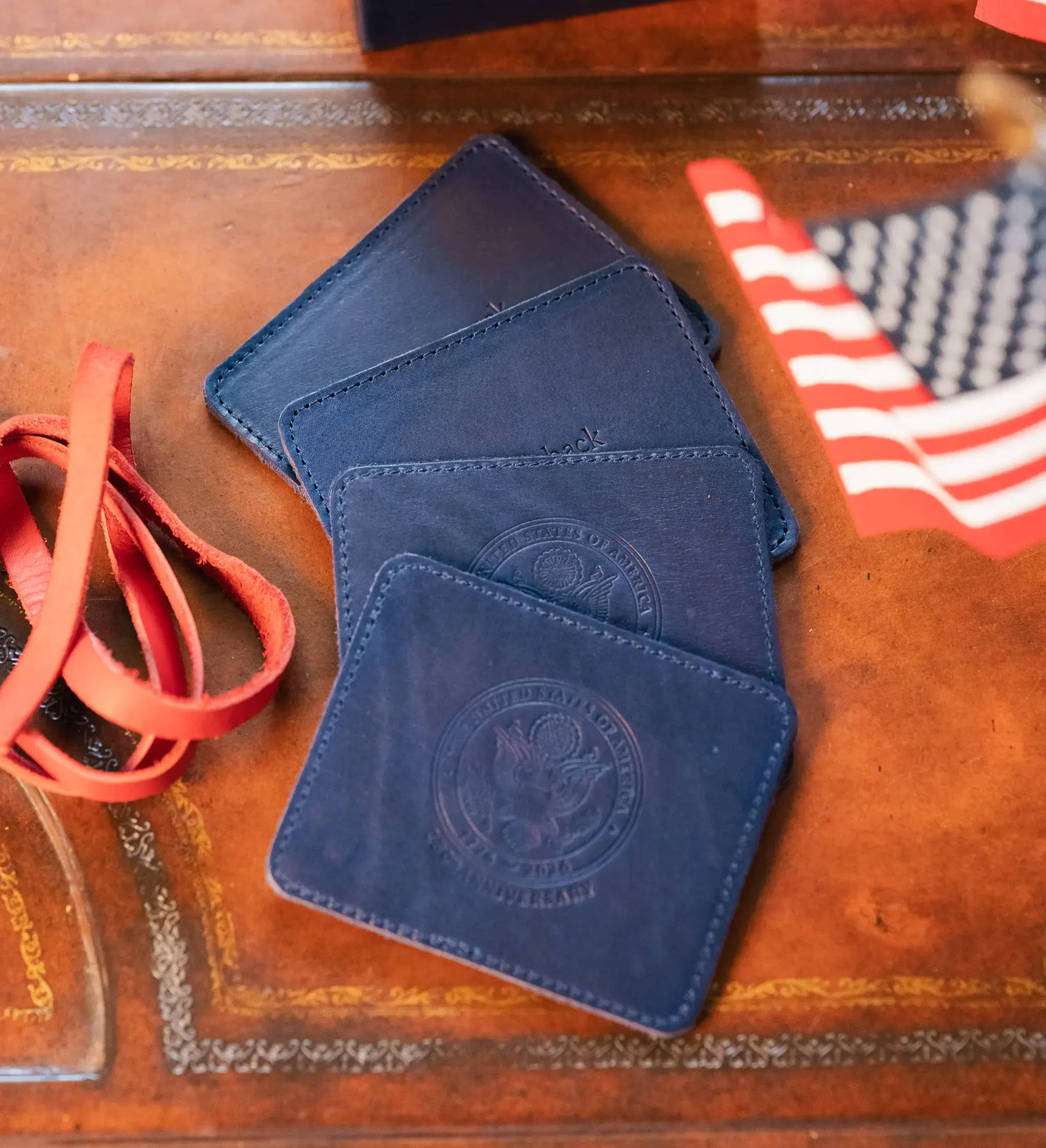 Four blue leather passport holders and a red strap on a wooden table.