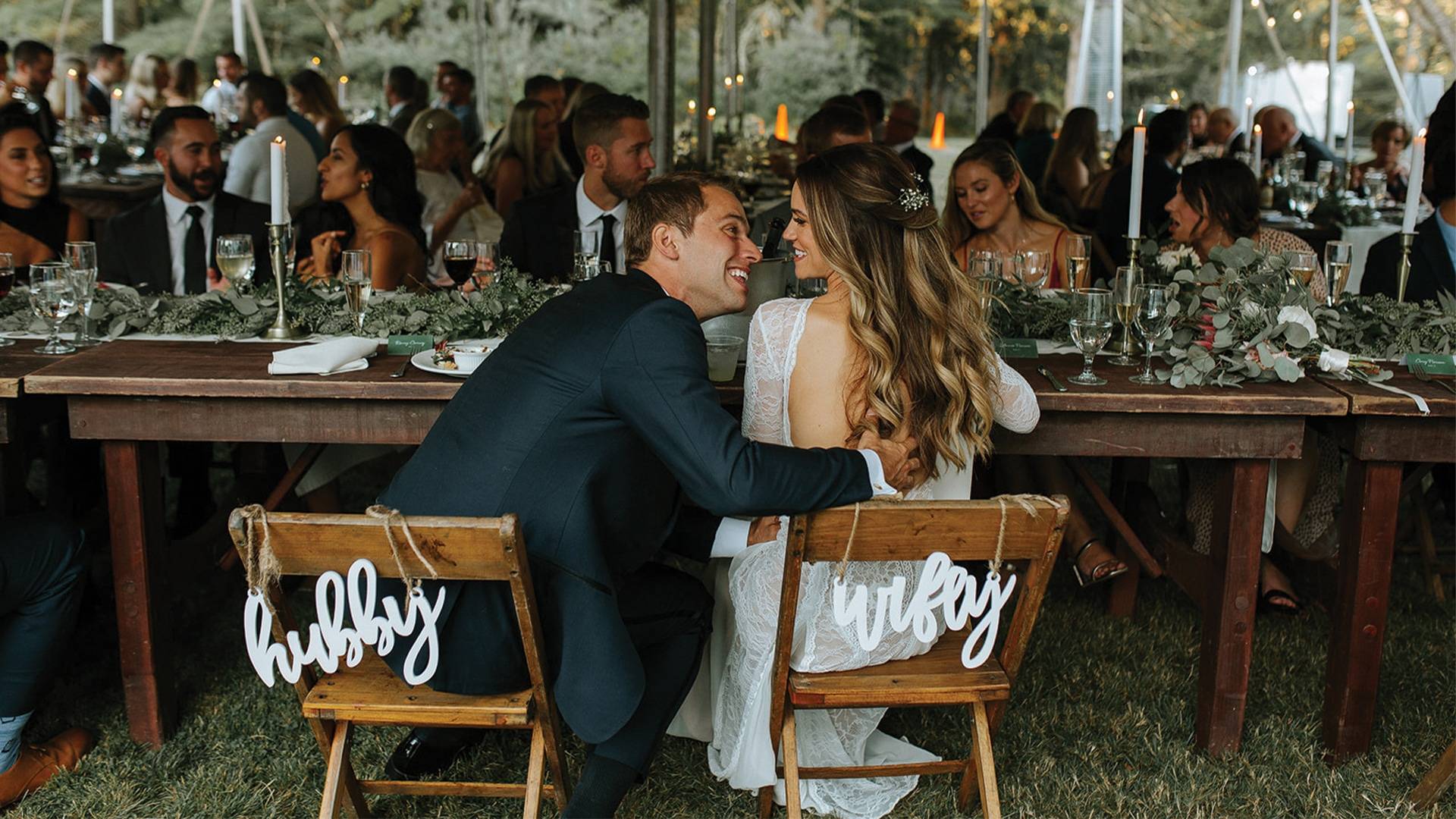 Bride and groom sitting on Hubby and Wifey wooden chairs