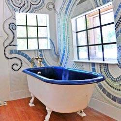 A bathroom with a claw foot tub and a mosaic wall in a swirl design.